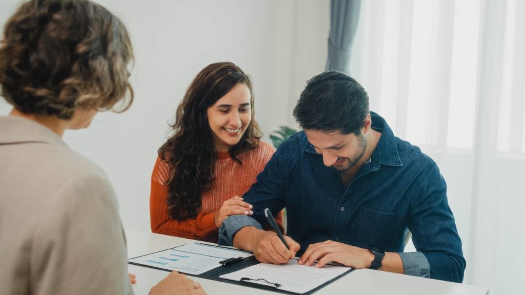 Young couple sit at desk signing documents together