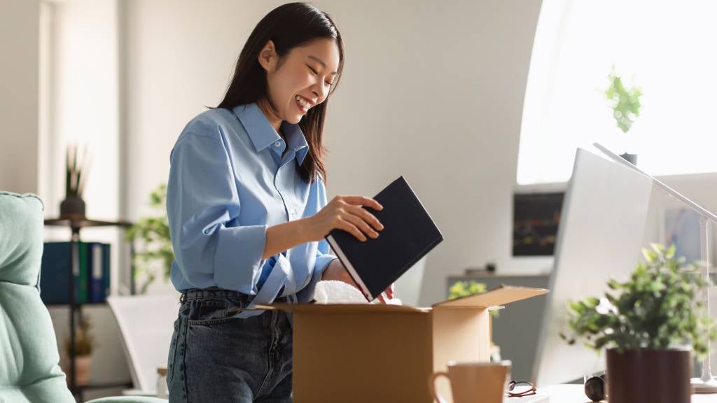 A smiling young woman unpacks her personal items on her new work desk