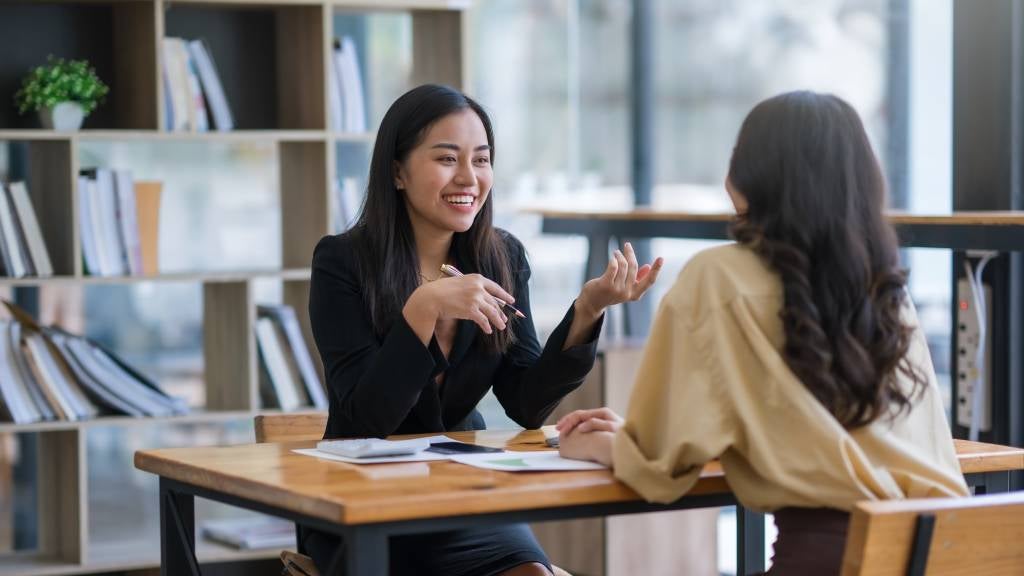 Two professional women sitting at a desk and having a discussion