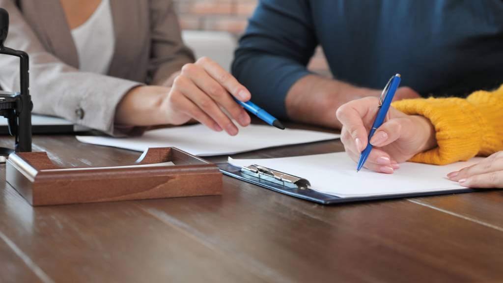 A close-up of hands showing a couple signing forms in front of a notary 