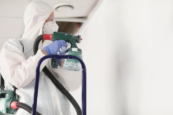 油漆工程行的油漆工穿防護服使用高壓噴槍朝牆面上漆