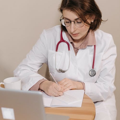 Doctor filling out a script in front of a laptop computer