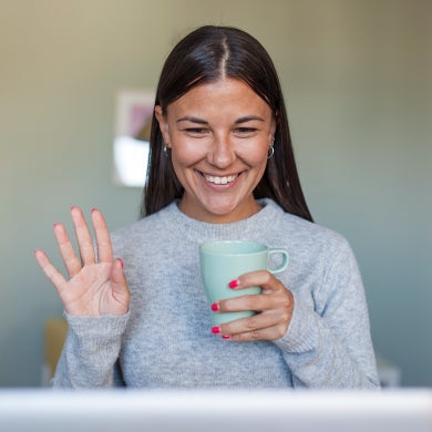 Woman holding a mug of coffee and smiling while looking at a computer screen during a remote consultation.