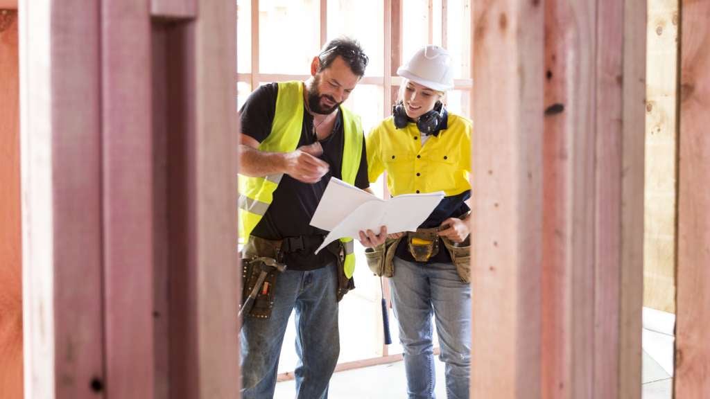 Two contractors stand together reading important documents at a construction site.