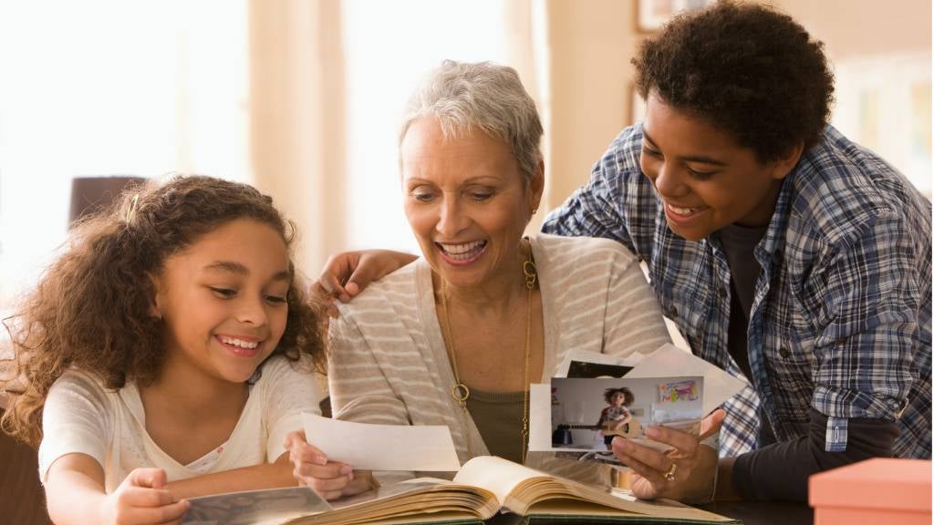 Happy young girl looking through photo albums with her sibling and grandmother.