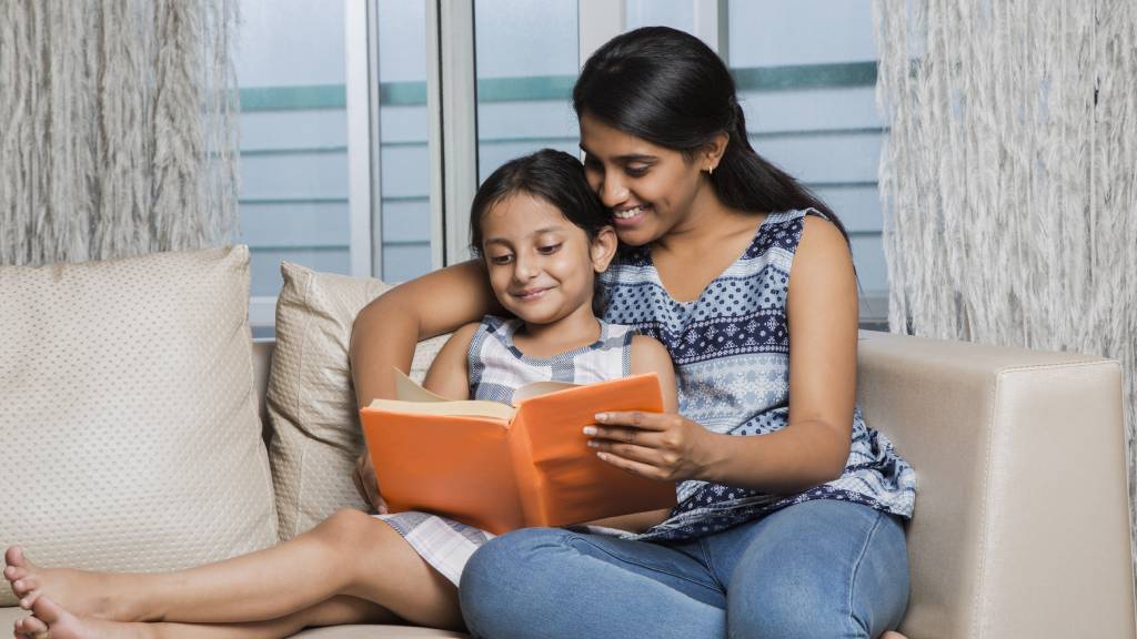 Mother and daughter reading a book at home on the couch