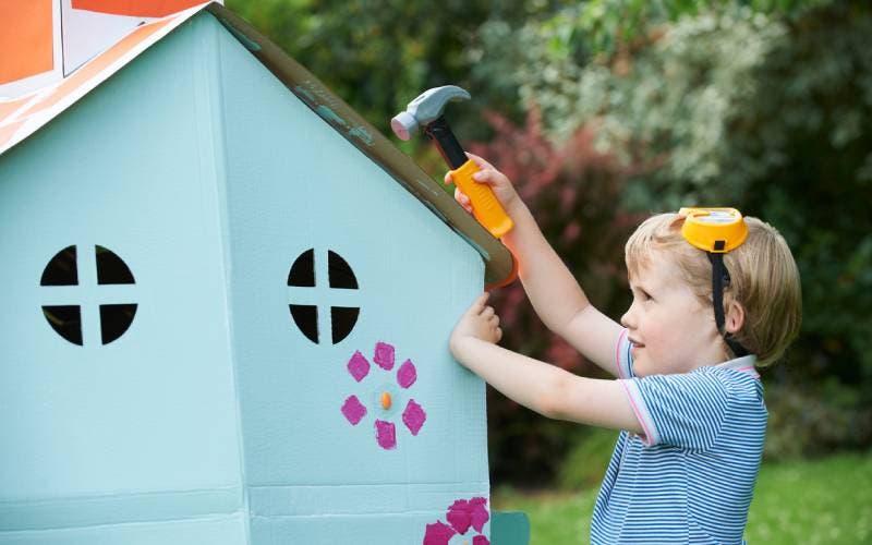 Young boy with toy hammer works on cubby house.