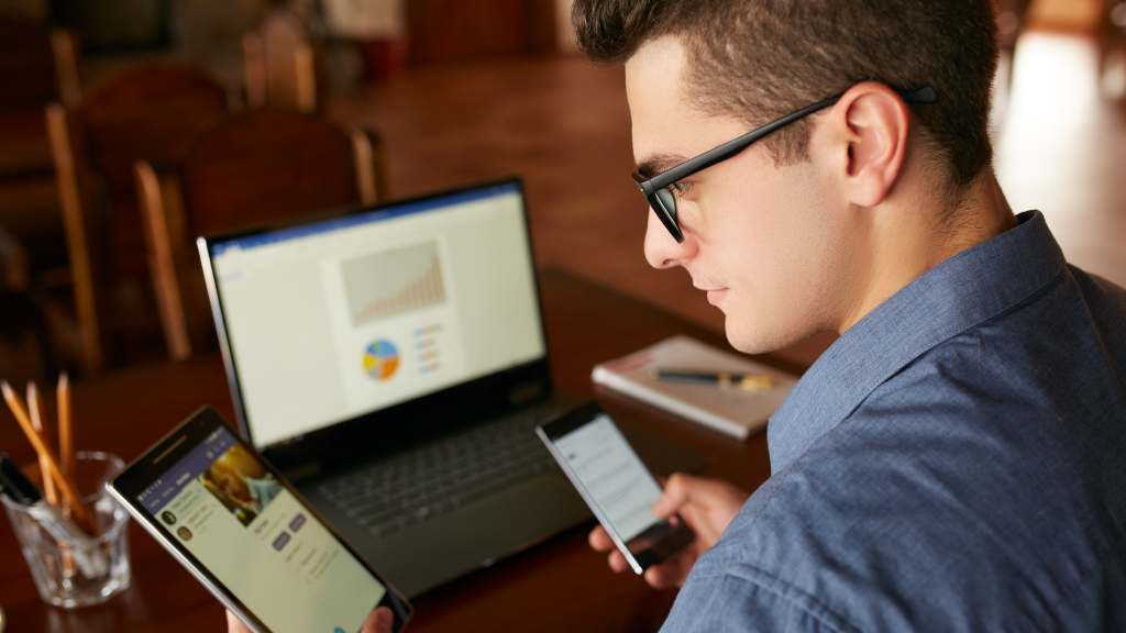 man using smartphone, tablet, and laptop simultaneously