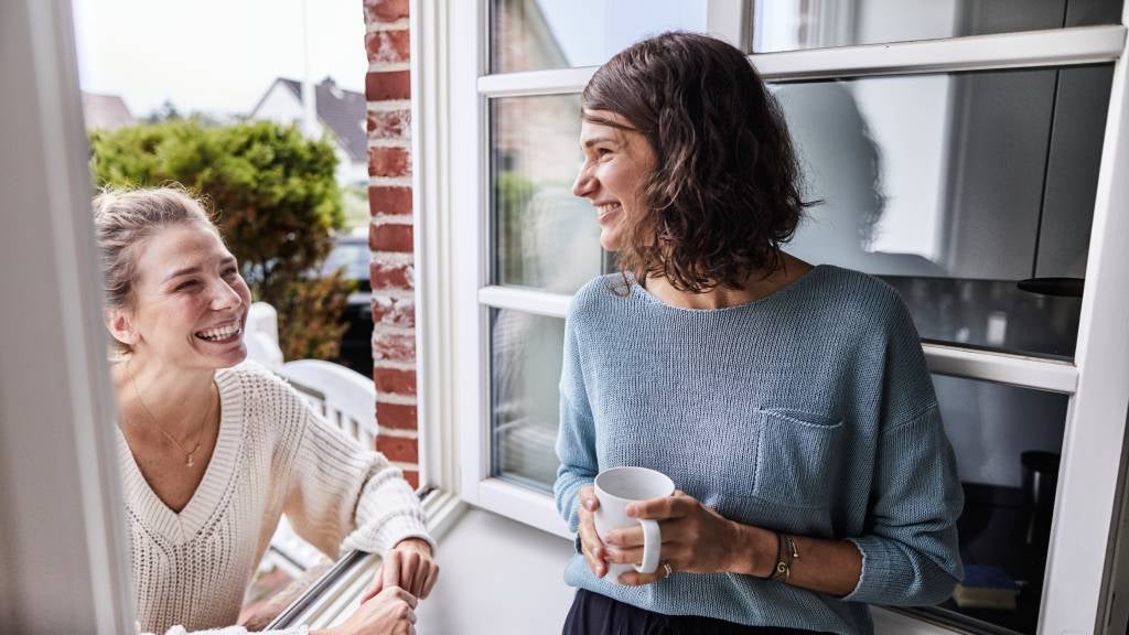 Two happy female neighbours talking through the window