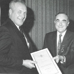 A black and white photo of two professional men holding out a certificate and smiling.