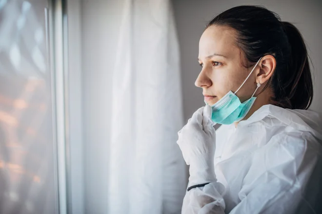 One woman, worried female doctor in protective suit, looking through the hospital window.
