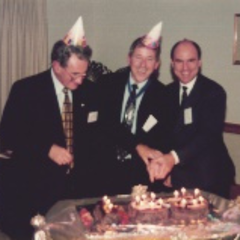 Three men smile while cutting a celebration cake.