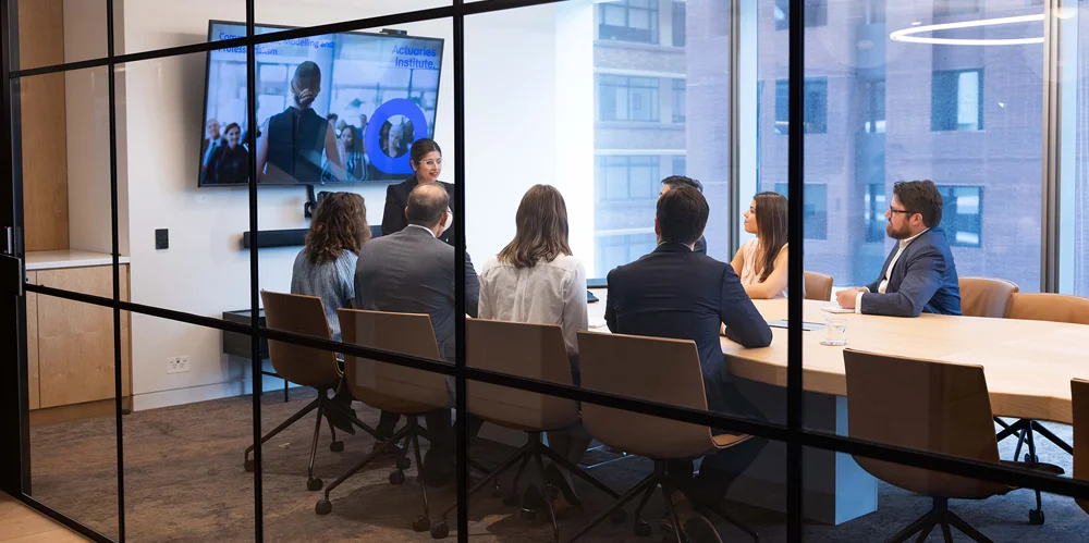 Actuaries sitting at a board table listening to someone present
