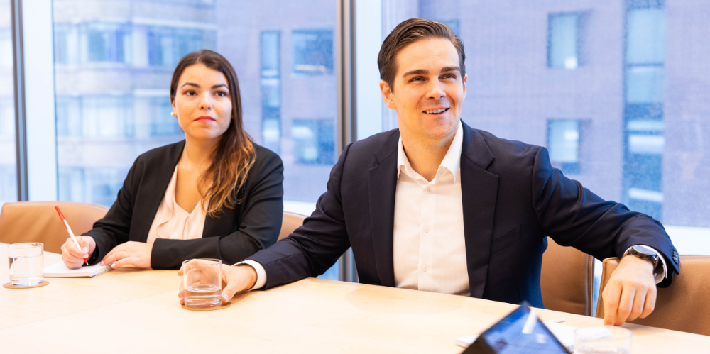 Young female and male business people sitting at desk looking past camera