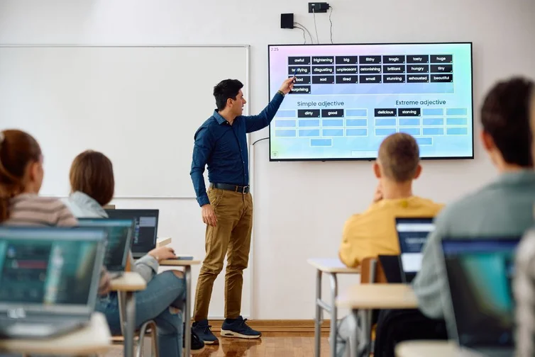 Teacher pointing to interactive board in high school classroom, students in foreground.