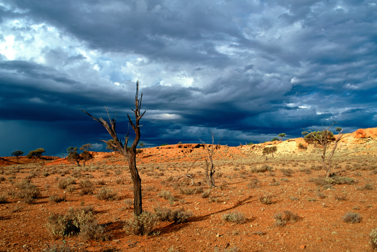 Harsh Australian desert juxtaposed to a dark, stormy sky.