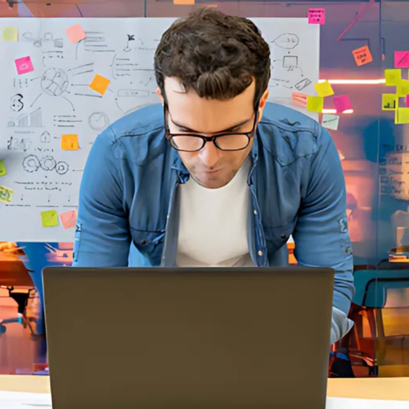 Man in blue shirt standing bent over laptop