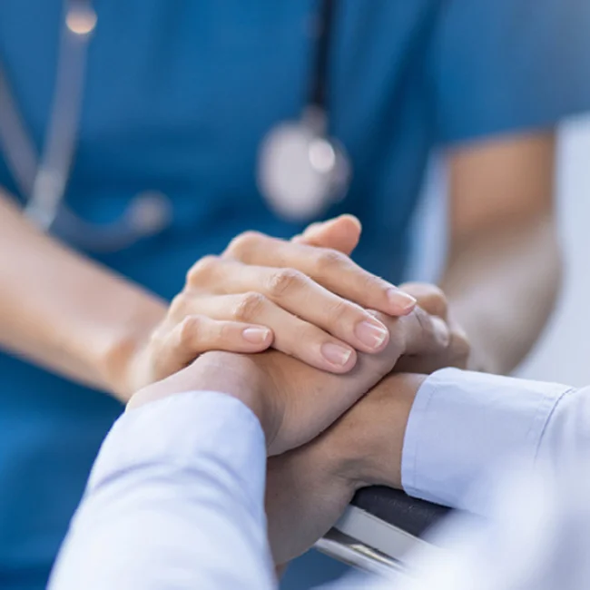 Health professional wearing scrubs and stethoscope holding hand of patient
