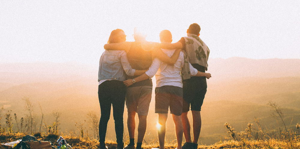 Group of four people hugging with backs to camera looking to the sunset