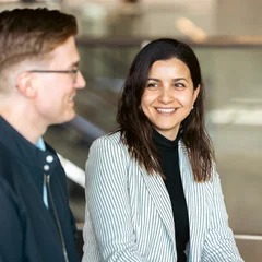 A man with glasses and a woman with brown hair and a striped blazer talking at event