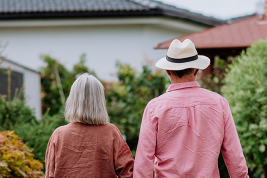 An older gentleman and women staying with their backs to the camera in front of a lush garden.