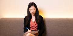 Woman sitting on grey couch writing on clipboard