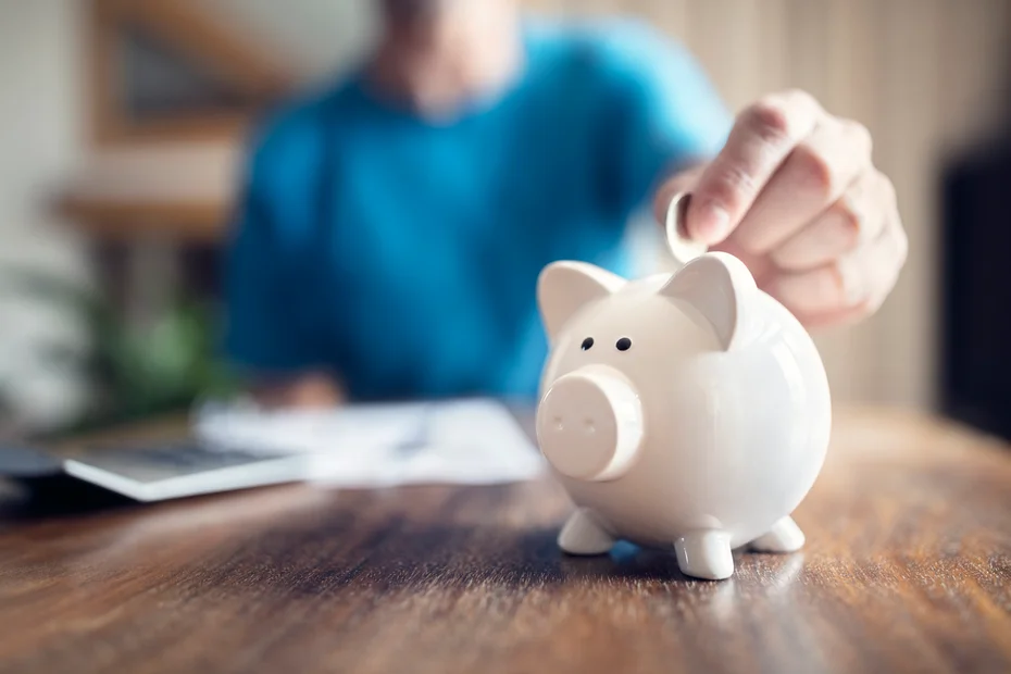 Man putting a coin into a pink piggy bank concept for savings and finance