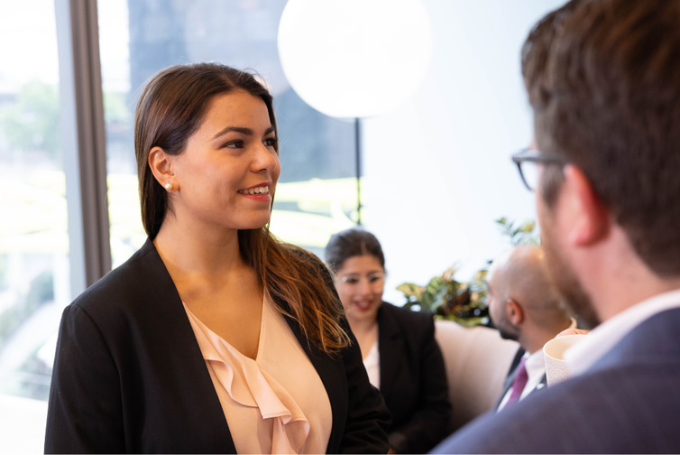 Young business woman with light apricot frilled shirt and black jacket smiling and talking to people