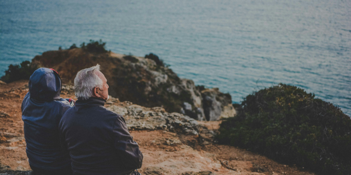 An older couple sitting on rocks, overlooking the ocean