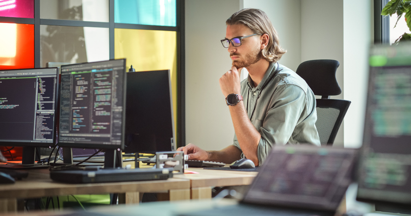 Focused man coding on desktop computer in stylish office space.