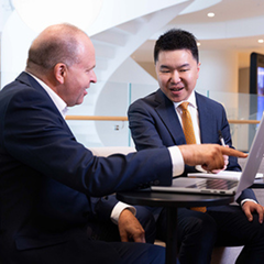 Two business men sitting and talking together, pointing to a computer screen