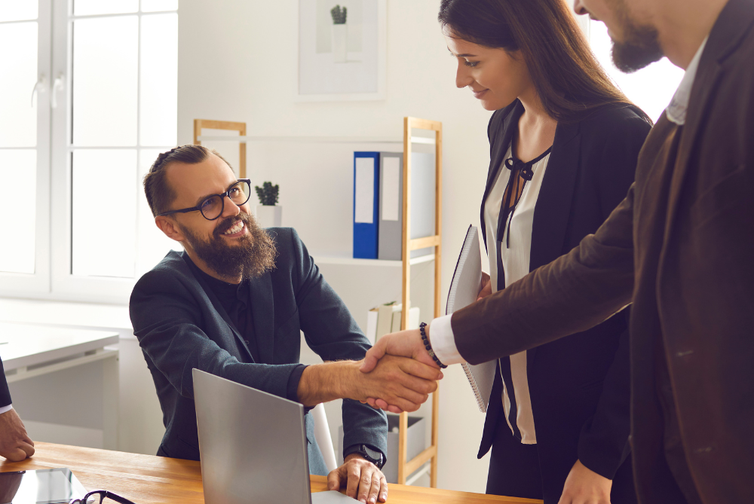 Man sitting down in office and shaking hand with people standing