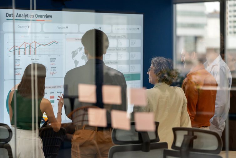 Collective group of co-workers looking at a large screen, analysing trends.