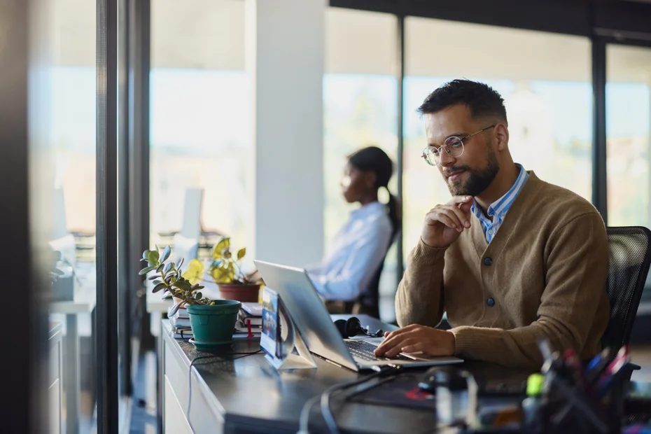 Young male design professional brainstorming while working on a computer in the office. His colleague is in the background.