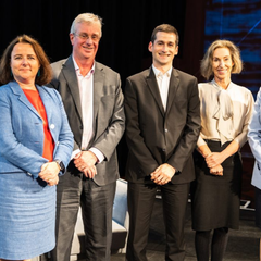Two men and two women in professional dress stand in a line smiling at the camera.