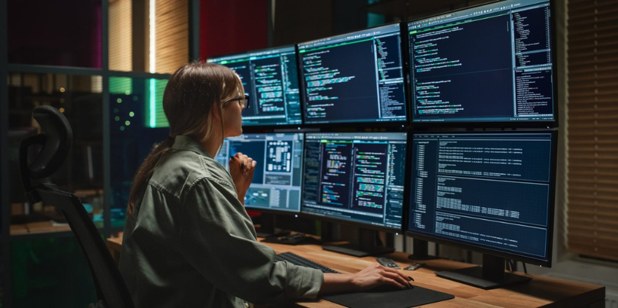A woman looking at her 6 monitors, for what could only be a very busy day at work