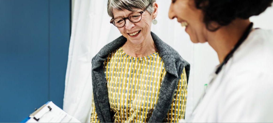 Patient and doctor smiling, doctor is holding clipboard.