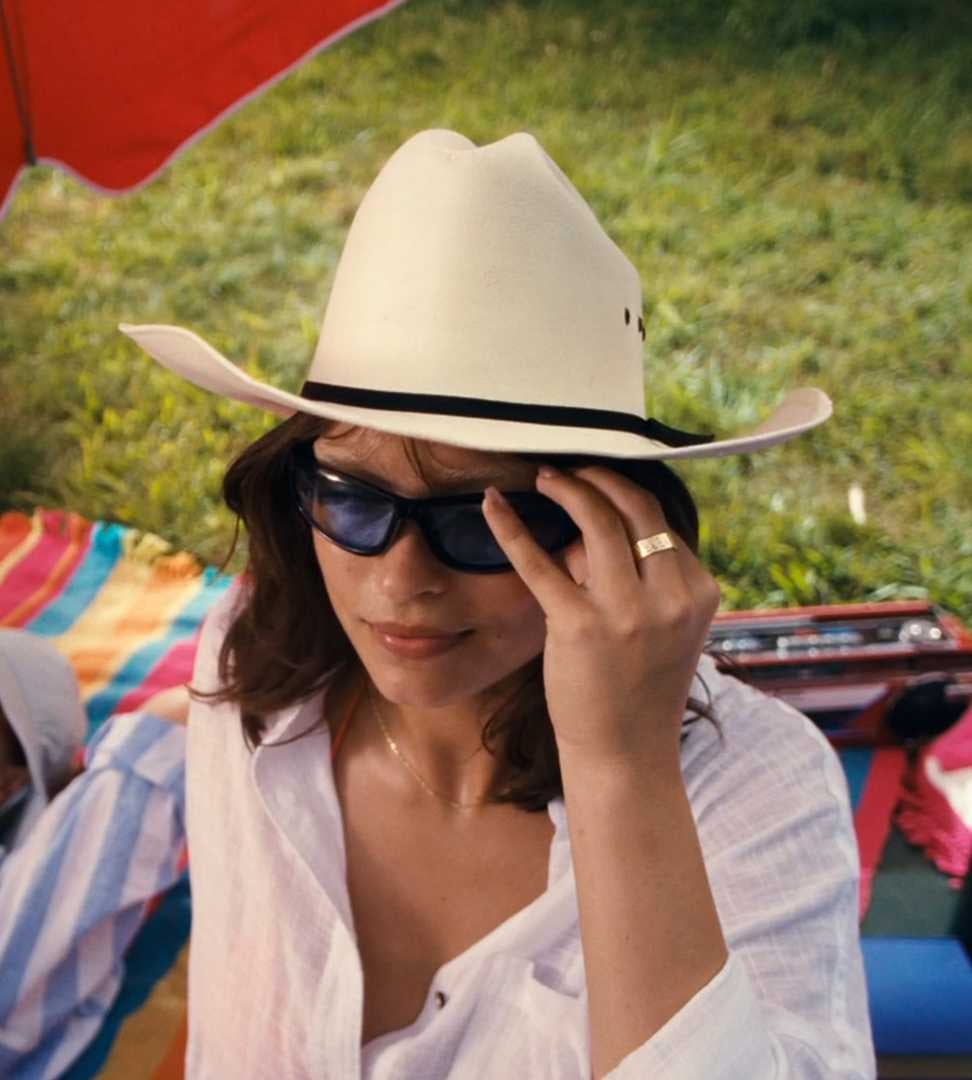 Woman wearing a hat and sun glasses sitting on a picnic blanket.