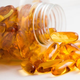 Orange capsule-shaped supplements spilling out of a clear jar.