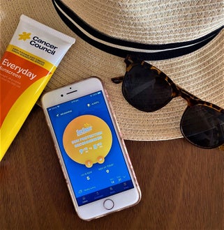 A hat, sunscreen tube, SunSmart app on iPhone and sunglasses.