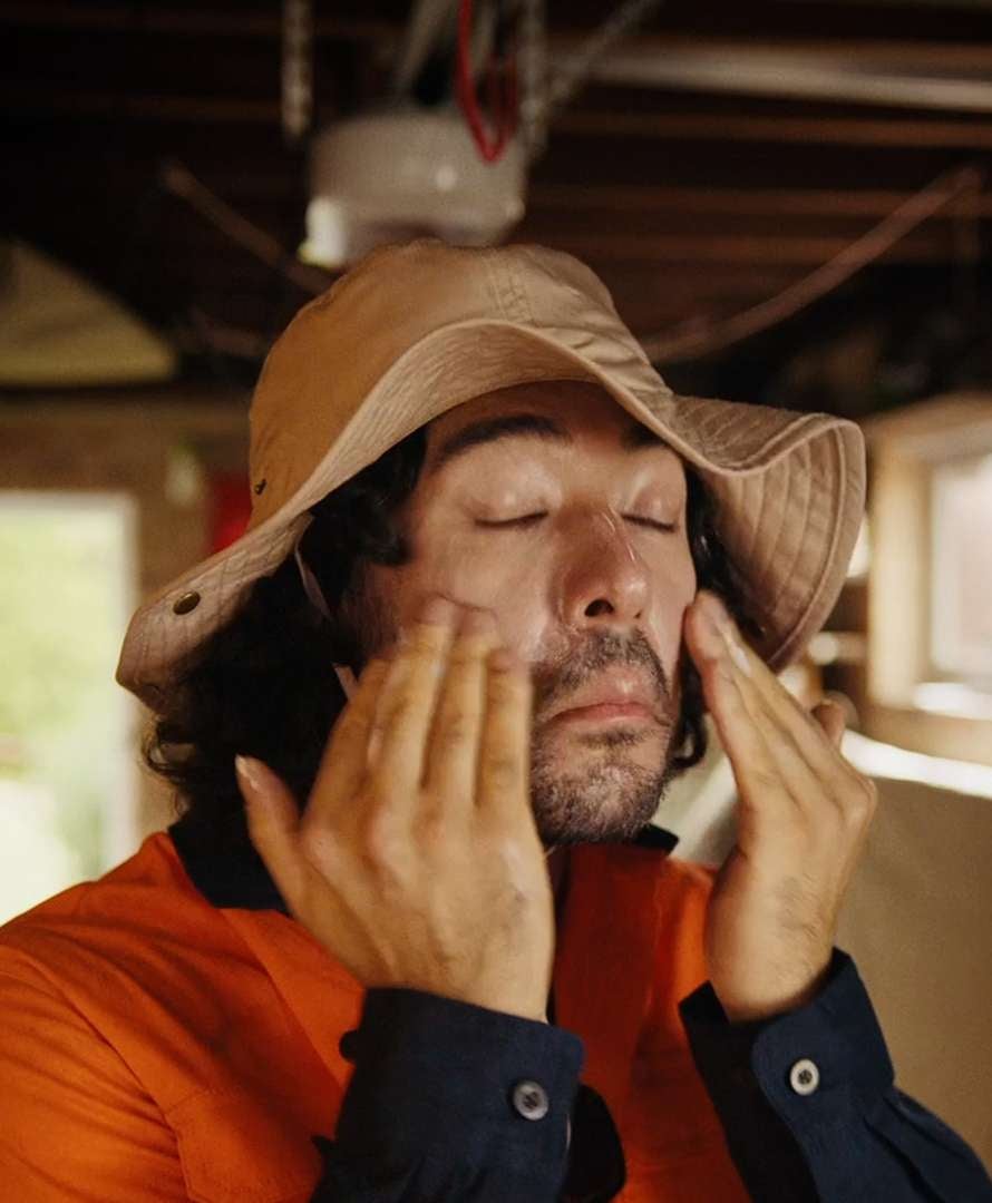 Man wearing a hat and a high-vis top applying sunscreen on his face. 