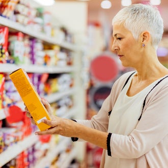 A woman in a supermarket aisle, reading a food label on a box of food.  