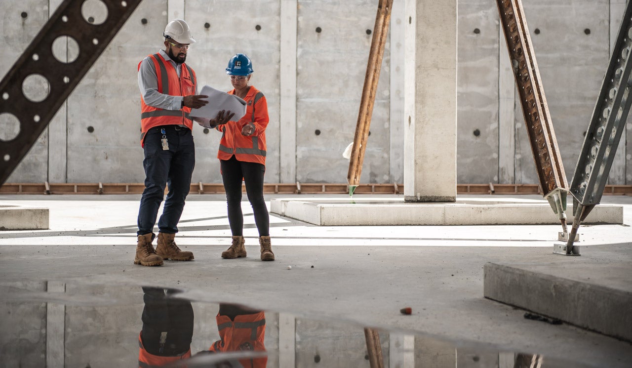 Inside the Pukekohe East Reservoir under construction - showing the scale of the project in comparison to Watercare staff and Fulton Hogan contractors looking over plans in the foreground.. 