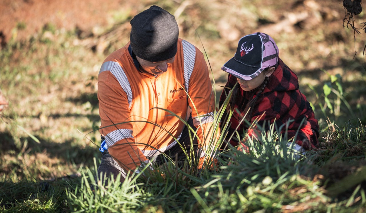 Watercare volunteer helps Ararimu School student plant a native tree on the riverbanks of a Hūnua tributary waterway.