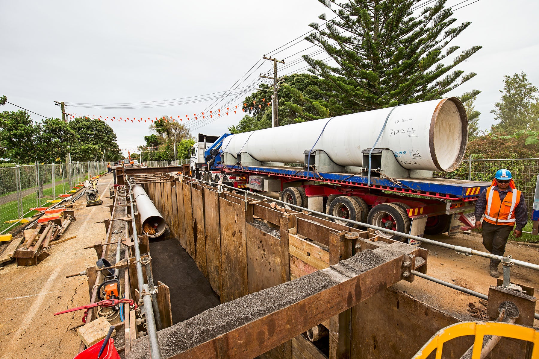 A huge water supply pipe for the Hūnua 4 watermain project arrives by truck beside a trench where it's ready to be connected.