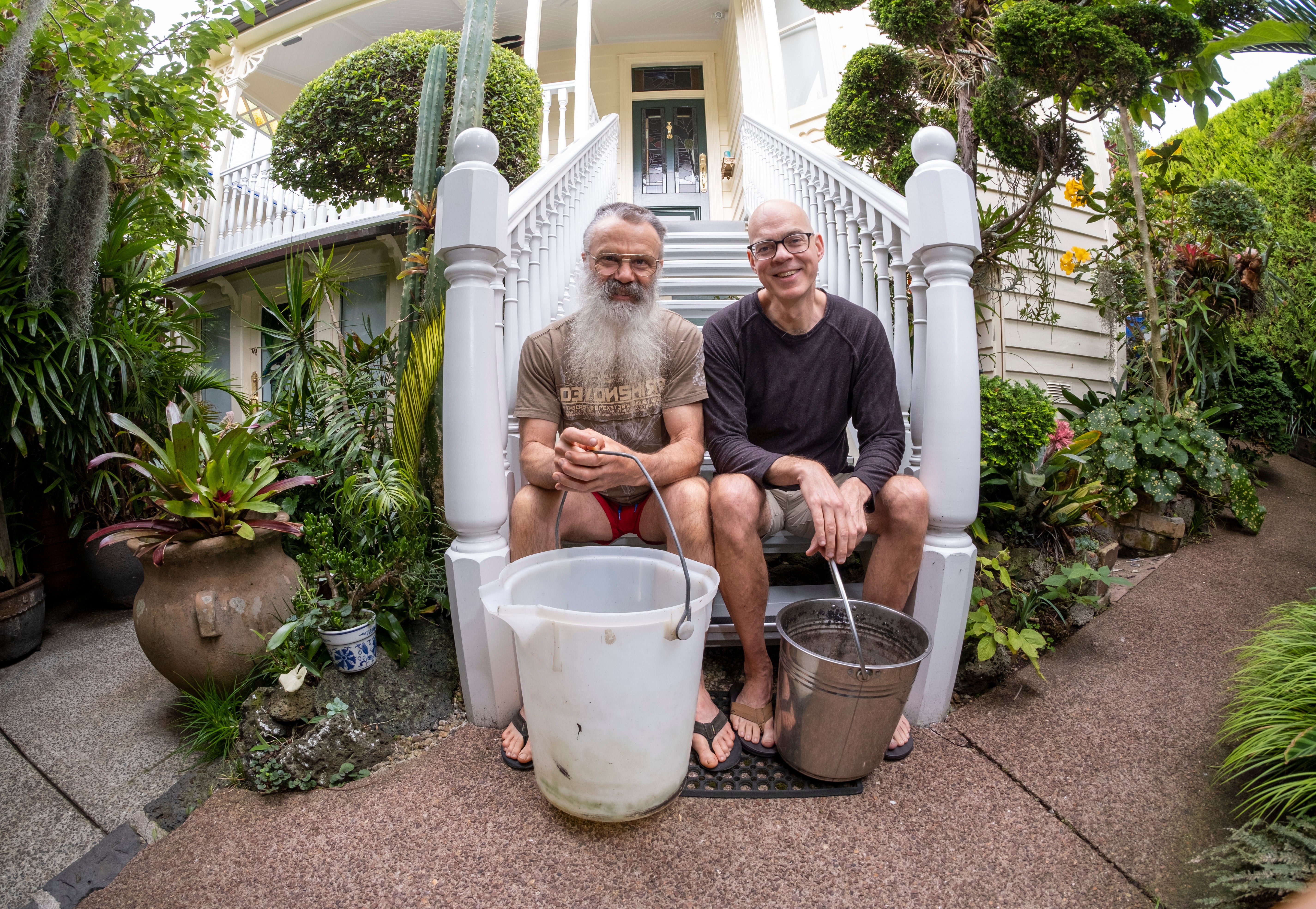 Mark and Gene sit on their front steps with buckets they use to water their garden.