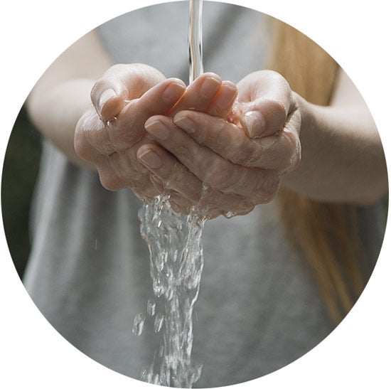 Photograph of water, flowing from above, spilling over and running through a woman's cupped hands.