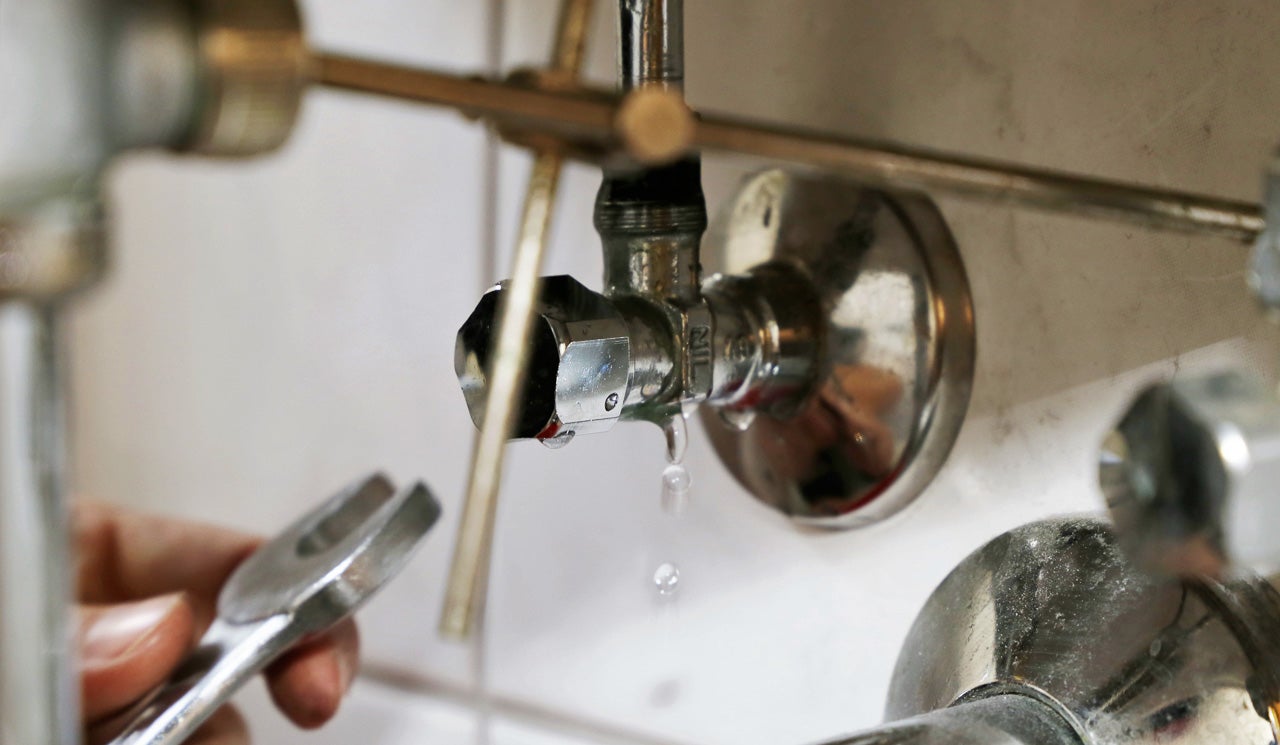 A spanner approaches a leaking tap fixture beneath the sink.