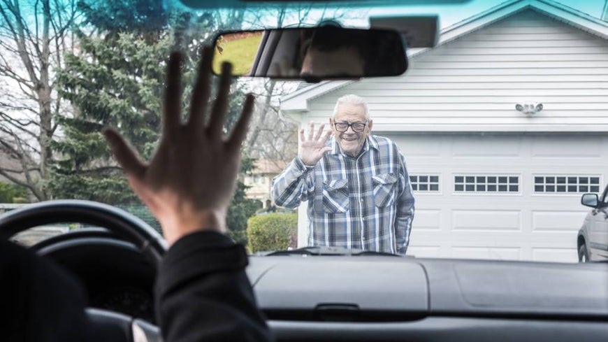 adult son waving to father from car