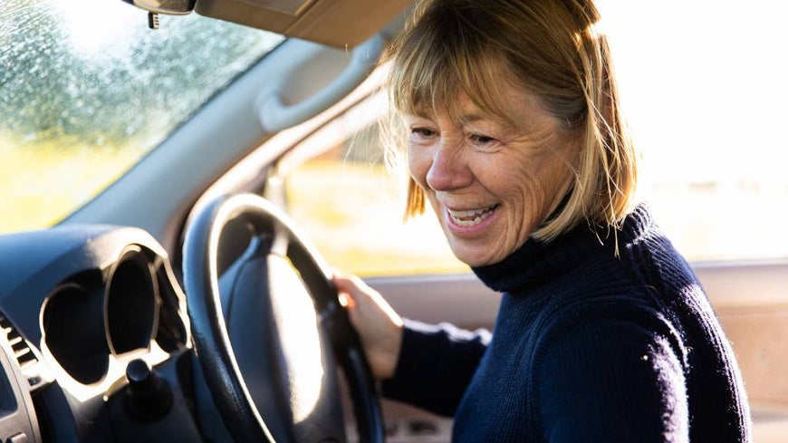 Over 50s female driver in turtleneck jumper at the wheel of her car. 